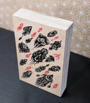 Black and red ink pattern style illustration on exposed wooden panel. The black elements are plant or bug inspired creatures, directioned like in flight. The red elements are like small amoeba creatures.