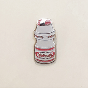 Gif of enamel pin of a small Yakult bottle packaging, white with red design accents. One image is of pin glowing in the dark and one is of pin in light.