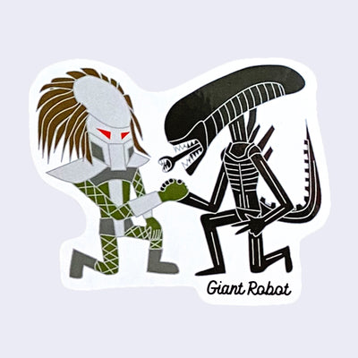 White cut out sticker with a cartoon version of Predator and Alien (from Alien vs Predator movies) kneeling and clasping hands with one another. "Giant Robot" is written in small cursive writing in bottom right.