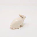 White ceramic rabbit, with simplistic body shapes and no facial features. It is positioned on all 4 paws, slightly sitting back with a gray smudged tear running from where its eye would be. Its ears are slightly back.