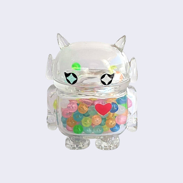 Soft clear vinyl figure with colorful round beads inside. Figure is shaped like a smaller Big Boss Robot, with a bigger head than normal and two black eyes with sparkles as pupils. A red heart is on its upper right chest.