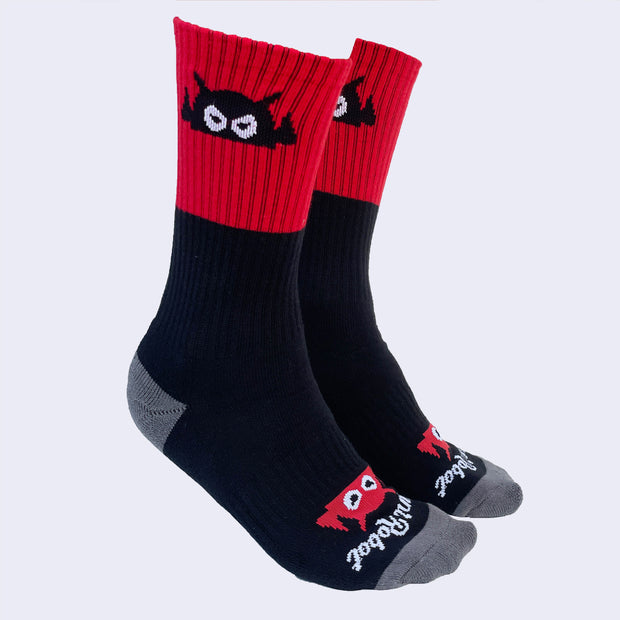 Side view of model's feet wearing red and black socks. A cartoon robot head decorates the sock's cuff. It peeks out when you wear sneakers.