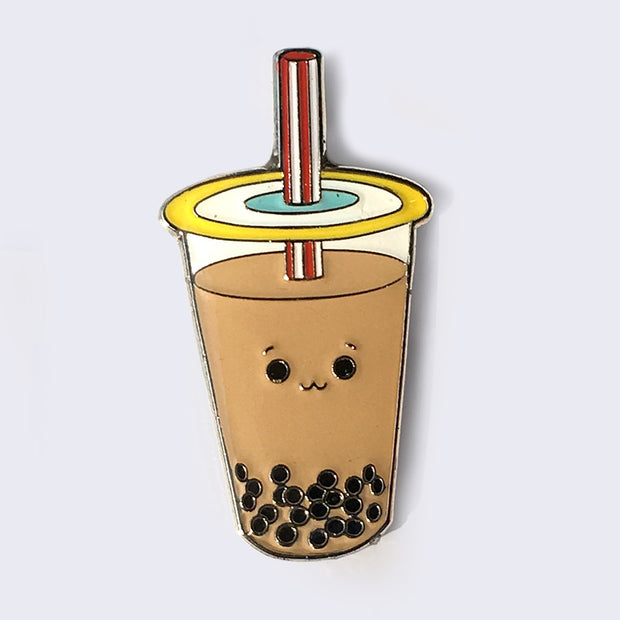 Enamel pin of a brown, milk tea boba cup with a small smiling face.