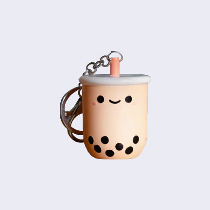 Small plastic sculpted keychain of a milk tea boba cup with a smiling cartoon face and a short pink straw, attached to a keychain.