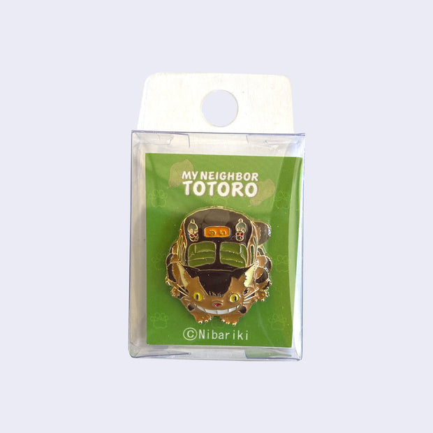 Enamel pin of a smiling Catbus, crouched down as if about to bound up. Pin is inside of a thin plastic case.