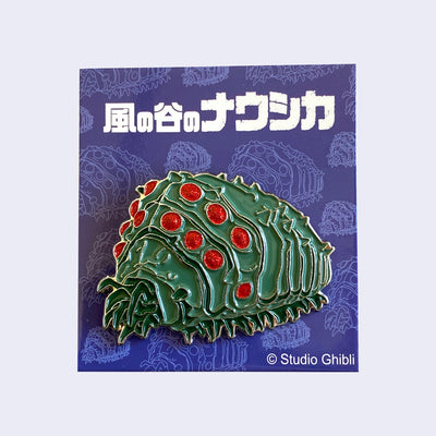 A brooch of a large, green grub bug  with many legs and glittery red dots as eyes.