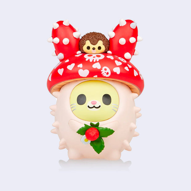 Vinyl bunny figure with a round, pastel pink body with spikes like a cacti. It's head is a red mushroom cap with white heart and skull patterns. It holds a strawberry plant in its hands and has a small brown hedgehog on its head.