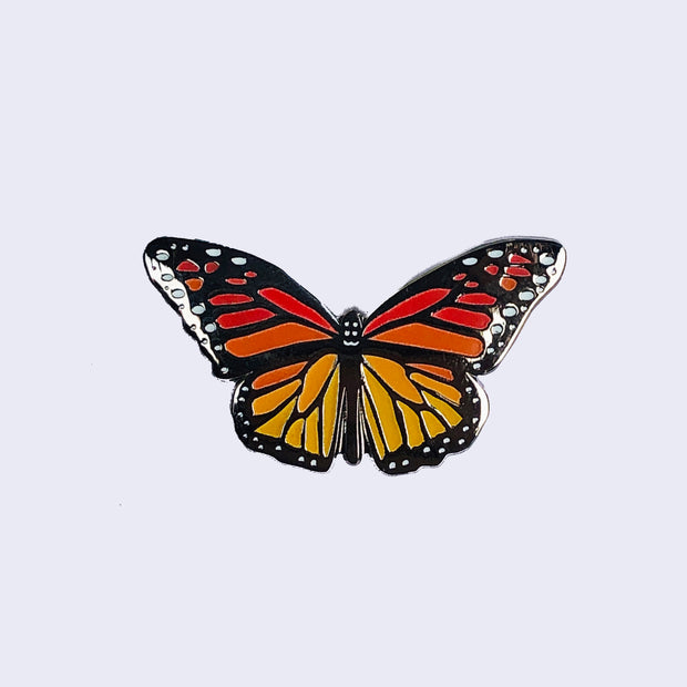 Enamel pin of a monarch butterfly, with a silver outline.