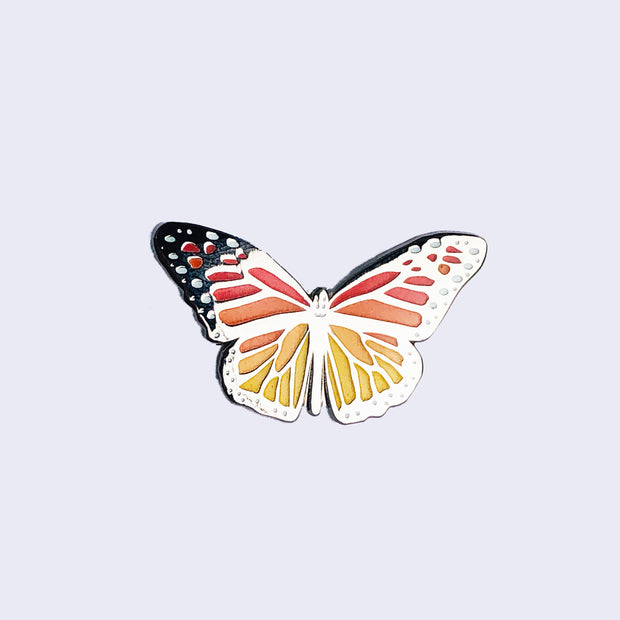 Side view of enamel pin of a monarch butterfly, displaying the metallic sheen of the pin.