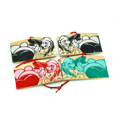 4 rectangular wooden tokens on red string, each with the same illustration of an anime style woman with a curvaceous body and bunny costume lingerie, looking back and exposing her butt that has a cotton bunny tail on it. She wears bunny ears and 2023 is written along the bottom. 2 tokens are black and white, 1 token is red and pink and the other is light and dark blue green.