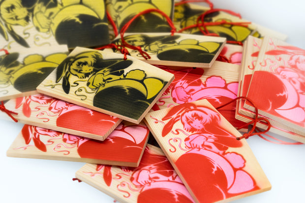 Stack of wooden tokens with the same spray painted image on them, either in black and gold or pink and red. Drawing is an anime style woman with a curvaceous body and bunny costume lingerie, looking back and exposing her butt that has a cotton bunny tail on it. She wears bunny ears.