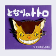 Enamel pin of a close up smiling Catbus face. On a purple backing card with Japanese writing.