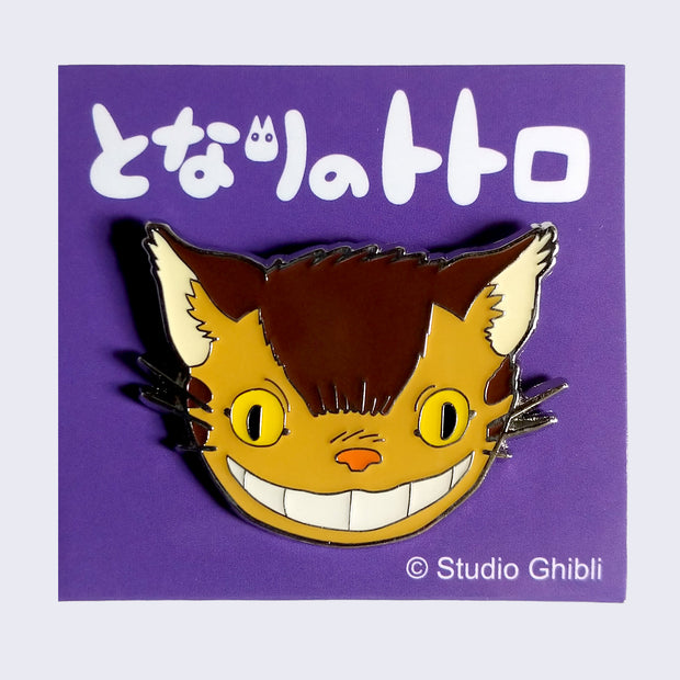 Enamel pin of a close up smiling Catbus face. On a purple backing card with Japanese writing.