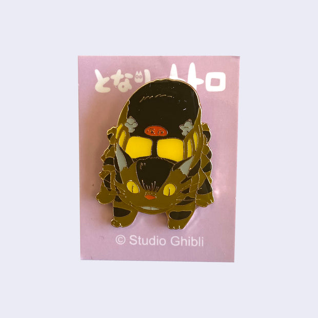 Enamel pin of Catbus with a slight smile, facing head on and looking down. On a light pink backing card with Japanese writing.