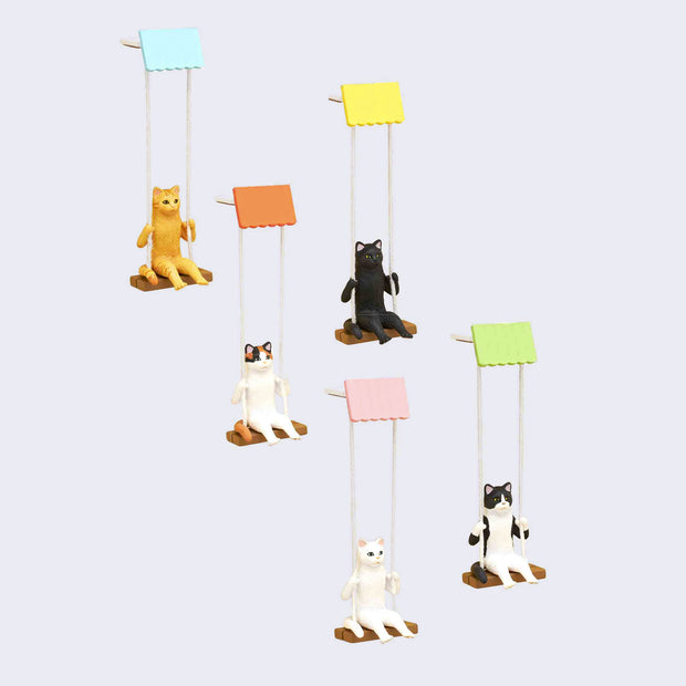 5 differently designed cat figurines, each sitting on their own wooden swing attached by string to a colorful top hanging base. Cat variations include: tabby, black, calico, white and tuxedo.