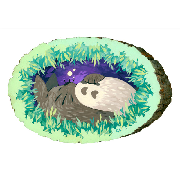 Painting of a sleeping Totoro, framed behind layers of leaves, as if the viewer is looking through a bush to peek on Totoro. Painting is on a wood slice with bark still on the edges. 