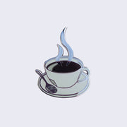 Enamel pin of a cup of black coffee, in a shallow white mug on a saucer with a spoon. Illustrated steam is coming up from the coffee. 