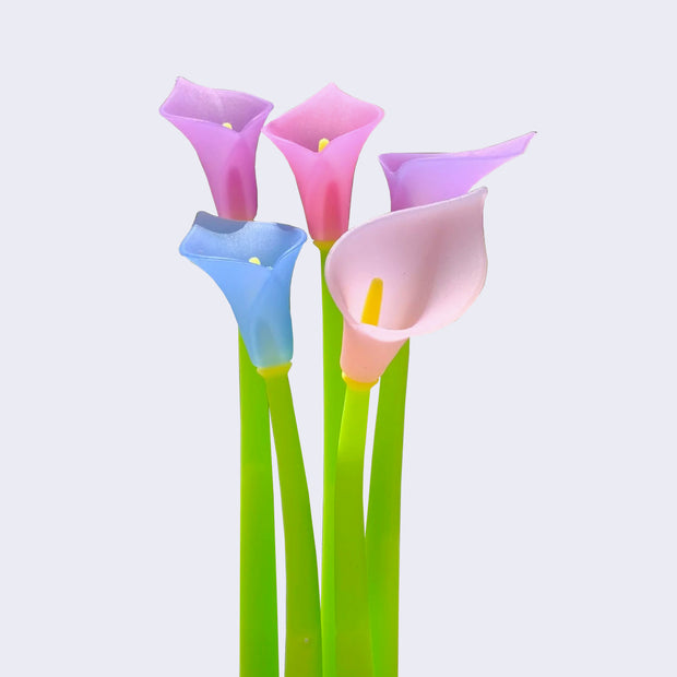Close up of 5 green rubber pens with calla lilies as pen toppers. Colors of lilies include periwinkle, violet, hot pink and light pink.
