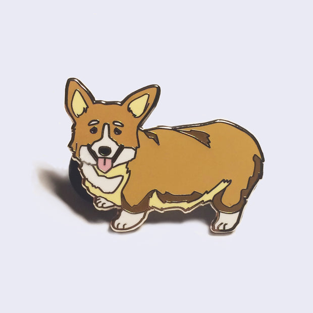 Enamel pin of an illustrated light brown corgi, standing with its tongue out and looking towards the viewer.