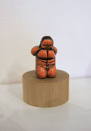 Sculpture of a nude person, kneeling and tied up in black rope bondage.