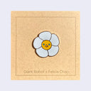 Enamel pin of a daisy with a smiling face