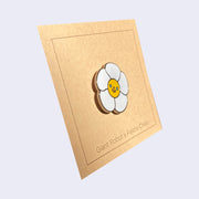 Side view of enamel pin of a daisy with a smiling face