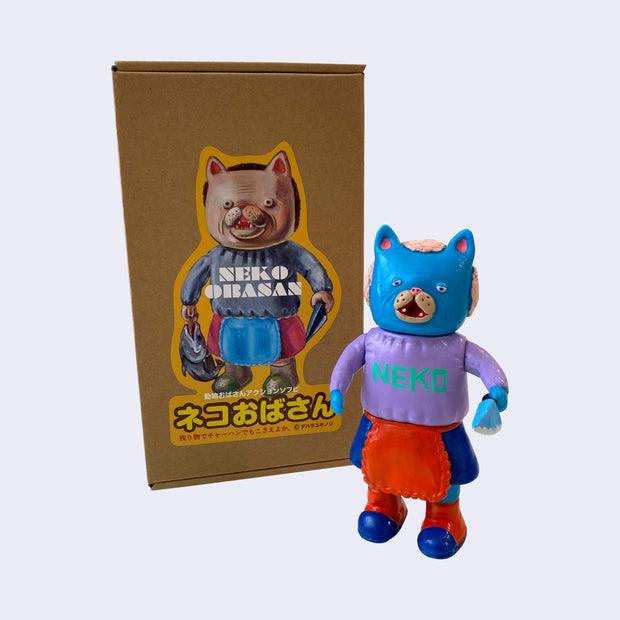 Blue painted soft vinyl figure of a cat headed humanoid with light pink hair, wearing a purple sweater that says "neko" and a blue skirt with a red frilly apron. She holds a blue knife.