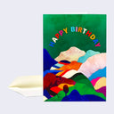 Greeting card with deep green background and many mountain ranges made out of colorful paper cuttings. "Happy Birthday" is written across the top in multicolor font.