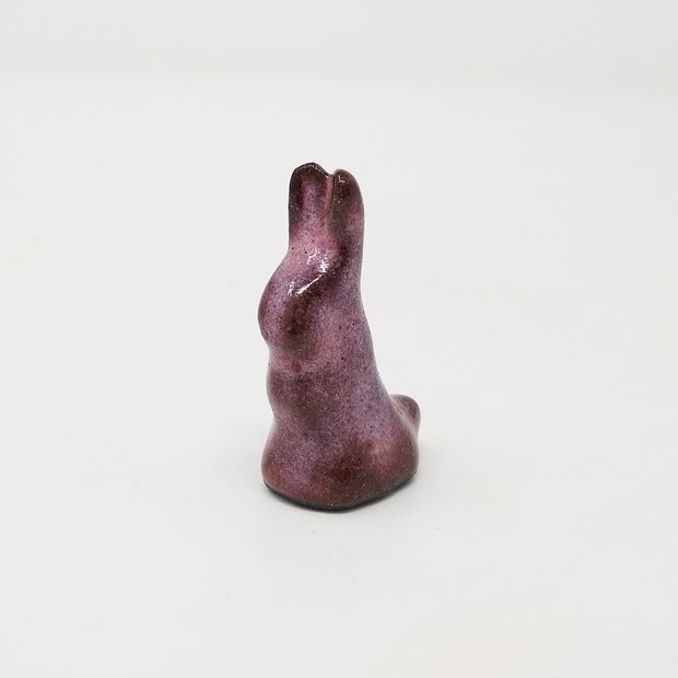 Aubergine purple ceramic rabbit, with very simplistic body shapes and no facial features. It is positioned upright with its ears straight up and small rounded tail.