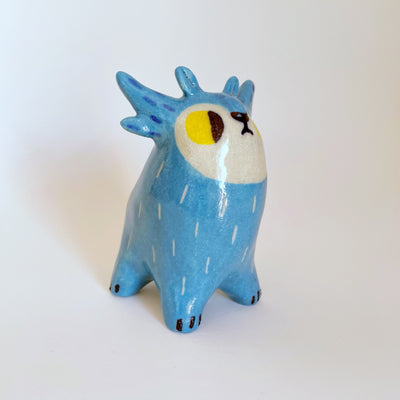 Small ceramic blue creature with abstract horns and a white face with yellow eyes, looking off to the side. 