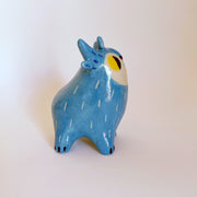 Small ceramic blue creature with abstract horns and a white face with yellow eyes, looking off to the side.