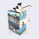 Small plastic fat cat, white with black spots, sitting on a box flat on its butt with its legs hanging down, holding a fishing pole made out of a thin branch. The box it sits on is its blind box packaging, which has photos of each different cat variation (tabby, calico, siberian cat, white with black and orange cat with folded ears).