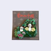 4 Kodamas on a green log that is wrapped in vines and covered in flowers. Brooch has glitter accents.