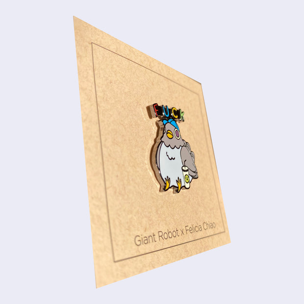 Side angle of enamel pin of a chubby, gray pigeon wearing a baseball cap and sitting next to a soda. "Fuck" is written above its head.