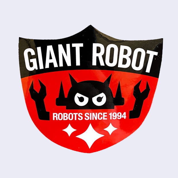 Red shield shaped sticker, with black top. "Giant Robot" is written in white bold font along top. A Big Boss Robot head is above "Robots Since 1994" with arms coming out of the text. 3 white sparkles are on the bottom.