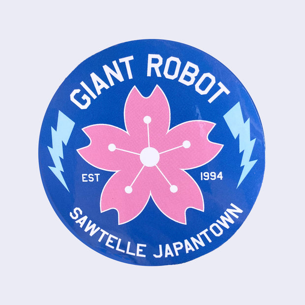 Blue circle sticker with "Giant Robot" written on top in white font and "Sawtelle Japantown" written on bottom. A pink cherry blossom is in middle with two blue lightning bolds on each side. 