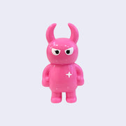 Hot pink colored vinyl figure character, standing with arms at its side. It has a round head with curved horns and simple angry eyes with no other facial features. It has a white sparkle on its upper right chest.
