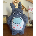A tall dark gray Totoro inspired plush. On a white patch on its stomach is a raincloud with water droplets and hearts coming down from it.