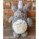 Plush crocheted doll of a chubby gray rabbit-bear creature with a small white ghost sitting atop its head and fishing.