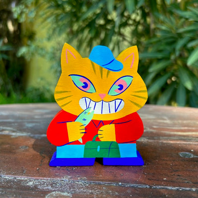Die cut painted wooden sculpture of an excited looking yellow cat, standing upright like a human. It wears a blue cap, red button up, jeans and blue boots and holds a green lunch pail in one hand and a fish in the other.