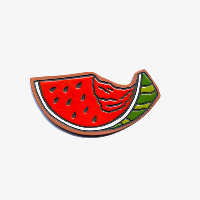 Earthenware die cut tile of a slice of watermelon with black seeds and a large bite taken out of it. A small amount of the green rind can be seen.