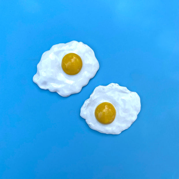 Two ceramic sunny side up eggs with fluffy egg whites and egg yolks on opposite sides for each egg.