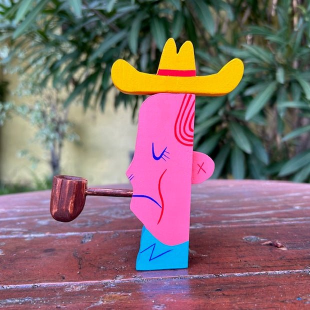 Die cut wooden sculpture of a mid western looking man, with a cowboy hat and smoking a pipe. It has its eyes closed and a slight frown.