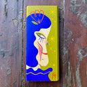 Olive green painted vertical rectangle piece of wood, with an illustration of a long faced blue haired girl looking off to the side.