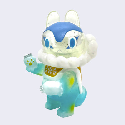 Soft vinyl figure of a Japanese style dog with a clear glitter head, blue facial accents and a fluffy white cloud scarf around its neck. Its body is light blue with white paws and it wears a golden cape with white lining.