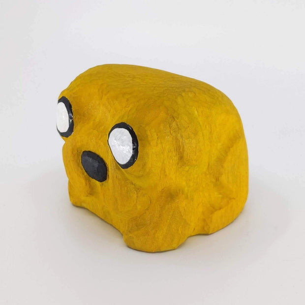 Whittled block shape wooden sculpture, painted yellow like Jake the Dog from Adventure Time. Only his eyes and nose are rendered.