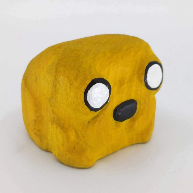 Whittled block shape wooden sculpture, painted yellow like Jake the Dog from Adventure Time. Only his eyes and nose are rendered.