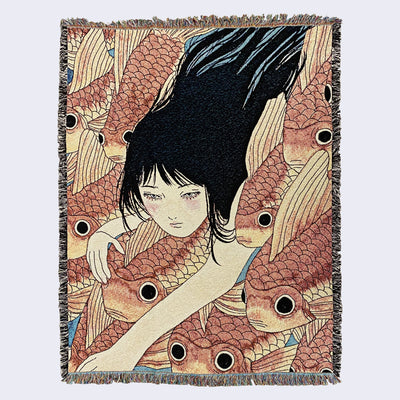 Large tapestry blanket with intentional frayed edges, rainbow on top and bottom and black and white on the sides. Tapestry design is of a pink cheeked woman with long black hair, swimming amongst orange koi fish. The blue of the water peeks out subtlety between her long hair and  in between the densely packed koi fish. 