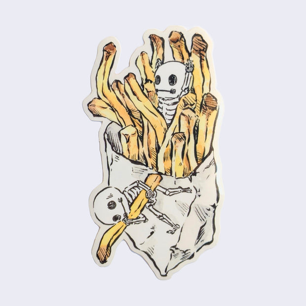 Sticker of an illustrated bag of french fries, with a small skeleton popping out of the middle and another small skeleton grabbing a fry outside of the bag.