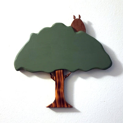 Simple wooden sculpture of a smooth surfaced tree, with a striped tree trunk and a wooden silhouetted Totoro in the top right of the tree.